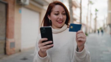 Genç kızıl saçlı kadın akıllı telefon ve kredi kartı kullanıyor.