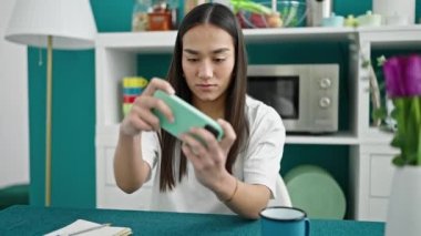 Genç, güzel İspanyol kadın yemek odasında akıllı telefonla video oyunu oynuyor.