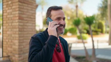 Orta yaşlı bir adam gülümsüyor. Sokakta akıllı telefondan konuşuyor.