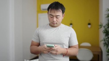 Genç Çinli adam evde akıllı telefon kullanıyor.