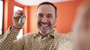 Orta yaşlı bir adamın yeni evinde elinde video kaydı var.