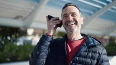 Middle age man smiling confident listening voice message by the smartphone at park