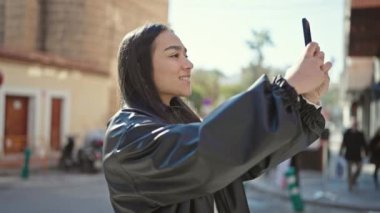 Genç, güzel, İspanyol bir kadın gülümsüyor. Akıllı telefonuyla caddede kendine güvenen bir video kaydediyor.