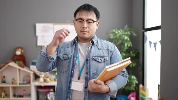 Young Chinese Man Teacher Smiling Confident Holding Books Kindergarten — Stok Video