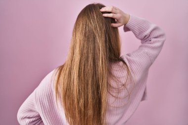 Pembe arka planda geriye doğru duran beyaz bir kadın elleri kafasında şüpheyi düşünüyor. 