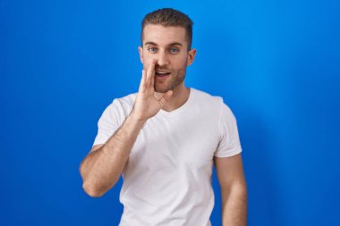 Kafkasyalı genç adam mavi arka planda el üstünde durup gizli dedikodular anlatıyor, kötü niyetli konuşmalar fısıldıyor. 