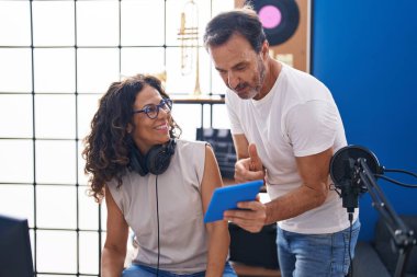 Man and woman musicians composing song using computer and touchpad at music studio