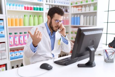 Genç İspanyol eczacı telefonda eczanedeki bilgisayarla konuşuyor.