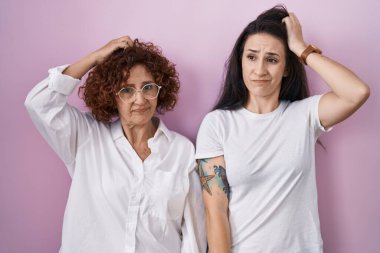 İspanyol anne ve kızı pembe arka planda günlük beyaz t-shirt giyiyorlar ve soru soruyorlar. Şüpheyle kararsız, kafa kafaya düşünerek. Düşünceli kavram. 