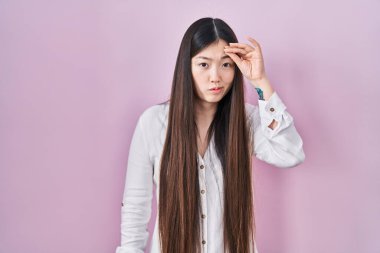 Chinese young woman standing over pink background worried and stressed about a problem with hand on forehead, nervous and anxious for crisis 