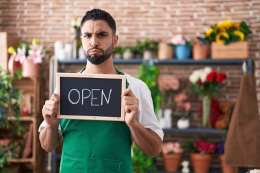 Çiçekçide çalışan İspanyol asıllı genç adam elinde komik yüzlü, şişen yanakları olan açık tabela tutuyor. Ağzı havayla şişer, havayı yakalar.. 