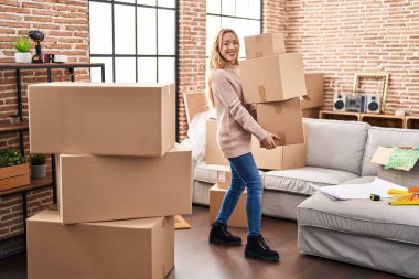 Yeni evinde paketleri tutarken kendinden emin gülümseyen genç kadın.