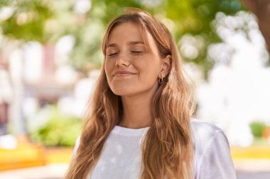 Young blonde girl smiling confident breathing at park