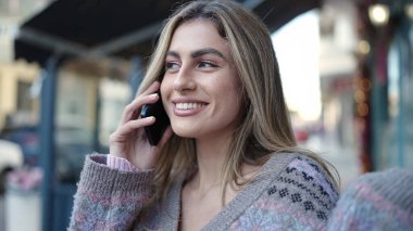 Genç sarışın kadın gülümsüyor. Kendine güveni tam. Akıllı telefondan konuşuyor.