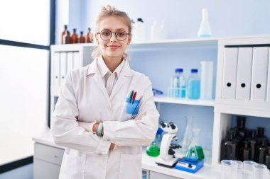 Young blonde woman scientist smiling confident standing with arms crossed gesture at laboratory