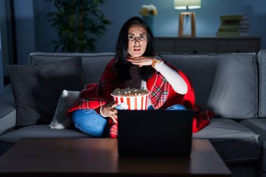 Kanepede film izlerken patlamış mısır yiyen, boğazını bıçak niyetine kesen, saldırganlığı şiddetle tehdit eden İspanyol bir kadın. 