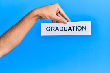 Hand of caucasian man holding paper with graduation word over isolated blue background