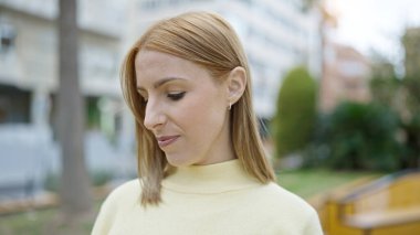 Young blonde woman looking to the side with serious expression at park