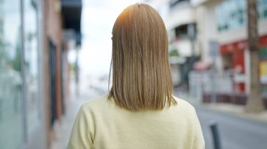 Young blonde woman standing backwards at street