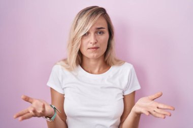Pembe arka planda duran genç sarışın kadın habersiz ve kolları açık, hiçbir fikri yok.. 