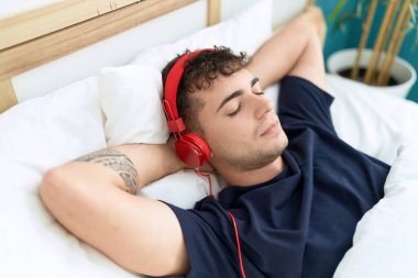 Young hispanic man listening to music relaxed on bed at bedroom