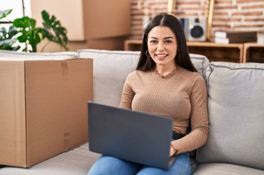 Young beautiful hispanic woman smiling confident using laptop at new home