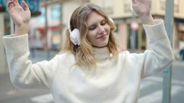 Young blonde woman listening to music and dancing at street