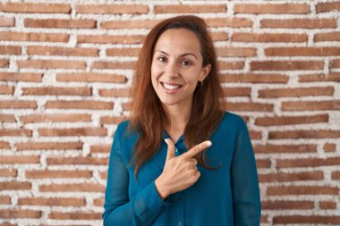 Esmer kadın duvarın üzerinde neşeli bir şekilde duruyor. Yüzünde mutlu ve doğal bir ifadeyle elleri ve parmaklarıyla gülümsüyor. 