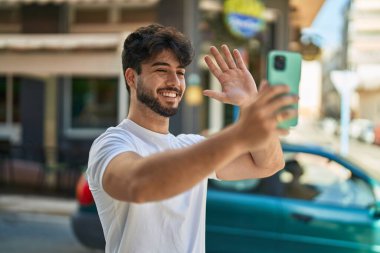 Young hispanic man smiling confident having video call at street