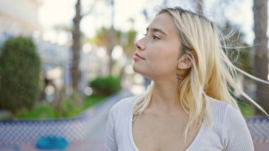 Genç, güzel, İspanyol bir kadın parkta ciddi bir ifadeyle yan tarafa bakıyor.