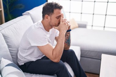 Young hispanic man stressed sitting on sofa at home