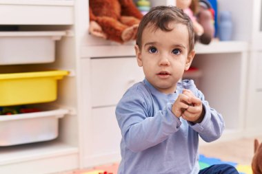 Anaokulunda rahat bir ifadeyle yerde oturan sevimli İspanyol çocuk.