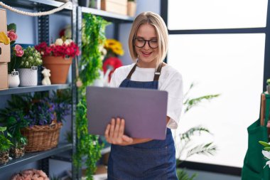 Çiçekçide dizüstü bilgisayar kullanarak gülümseyen genç sarışın kadın.