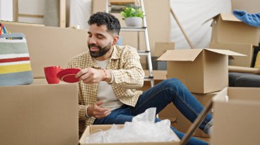 Young hispanic man unpacking cardboard box at new home