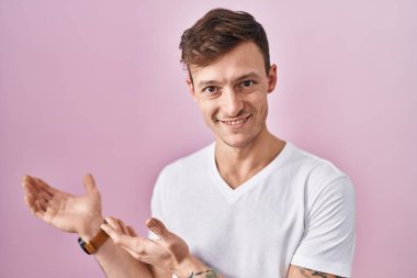 Pembe arka planda duran beyaz adam gülümseyerek doğal bir şekilde içeri girmeye davet ediyor. 