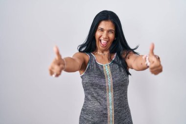 Beyaz arka planda durup olumlu jestler yapmayı onaylayan, gülümseyen ve başarı için mutlu olan olgun İspanyol kadın. kazanan jest. 