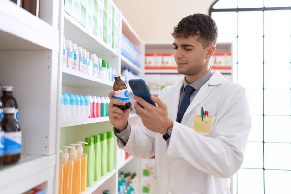 Young Hispanic Man Pharmacist Using Smartphone Holding Medication Bottle Pharmacy — Stock Fotó
