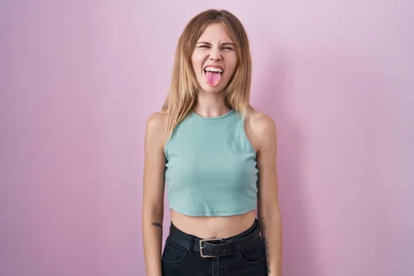 stock image Blonde caucasian woman standing over pink background sticking tongue out happy with funny expression. emotion concept. 