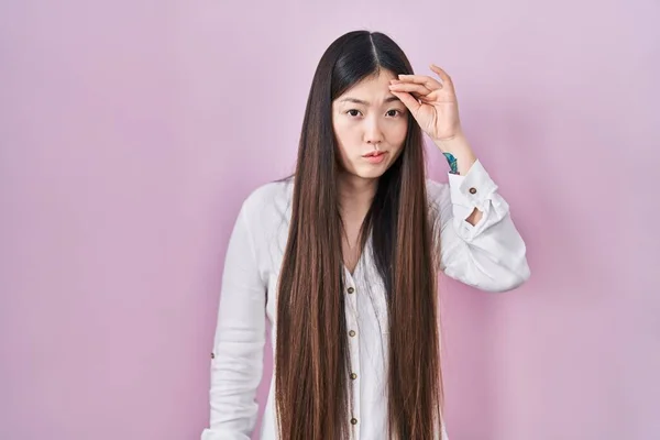 ピンクの背景に立っている中国の若い女性は心配し 額に手で問題について強調しました 危機への神経と不安 — ストック写真