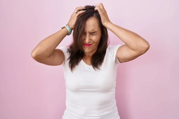 中年黑发女人站在粉红的背景上 由于疼痛和偏头痛 绝望和紧张 手放在头上 — 图库照片