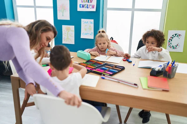 教室のテーブルに座って授業を受けている子供たちの女性とグループ — ストック写真
