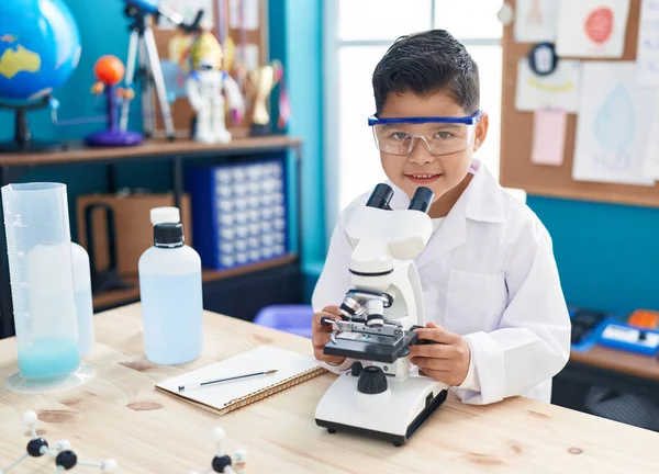 Laboratuvar sınıfında mikroskop kullanarak kendinden emin gülümseyen sevimli İspanyol çocuk.