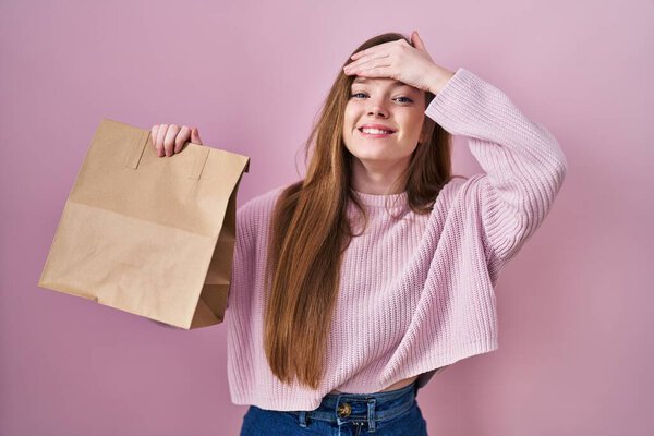 Young caucasian woman holding shopping bag and credit card stressed and frustrated with hand on head, surprised and angry face 