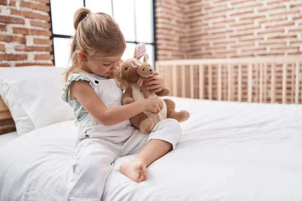 Stock image Adorable blonde girl playing with doll sitting on bed at bedroom