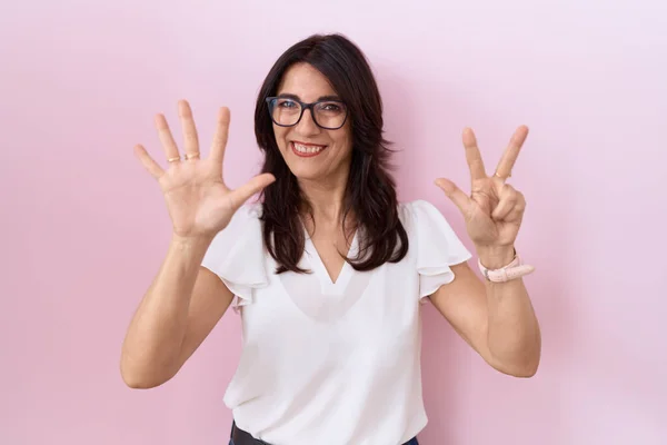 中世のヒスパニック女性を身に着けているカジュアル白いTシャツと眼鏡を表示し 指番号8で指摘しながら 自信と幸せ笑みを浮かべて — ストック写真
