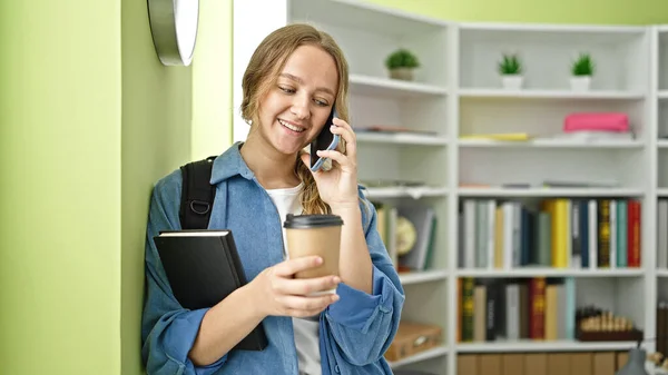Akıllı Telefondan Konuşan Genç Sarışın Kız Öğrenci Kütüphanede Kahve Içiyor — Stok fotoğraf