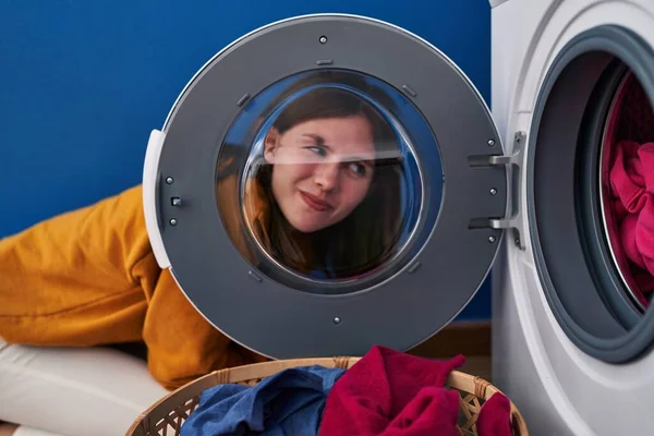 若いですブルネット女性見ますザ洗濯機の窓を通して笑顔側を見て離れて考えて見つめて — ストック写真