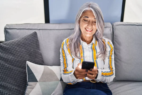 Kobieta Średnim Wieku Siwe Włosy Pomocą Smartfona Siedzi Kanapie Domu — Zdjęcie stockowe