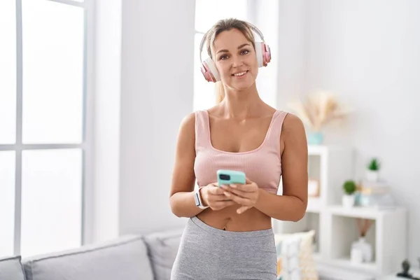 stock image Young blonde woman listening to music using smartphone at home