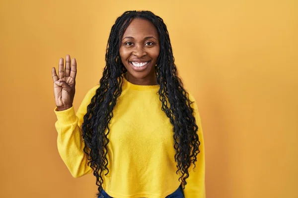 非洲妇女站在黄色的背景上 用四号手指指指指点点 自信而快乐地微笑着 — 图库照片